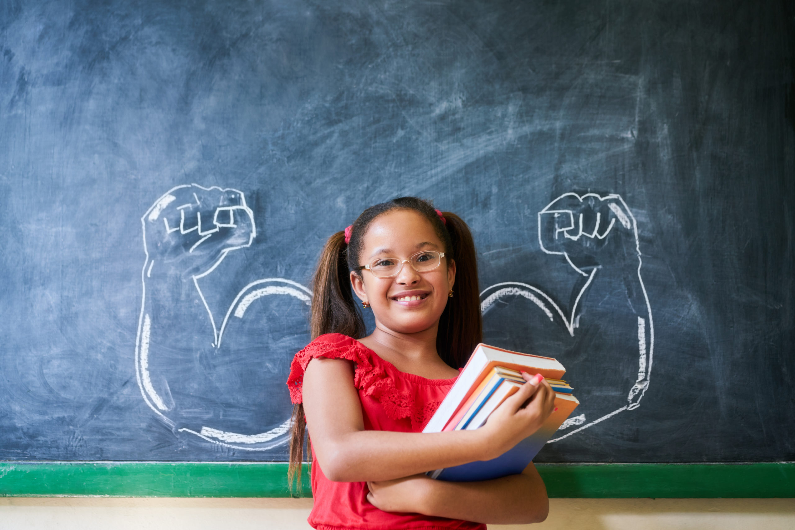 Smiling young student stands in front of a chalkboard with giant muscles drawn on it.