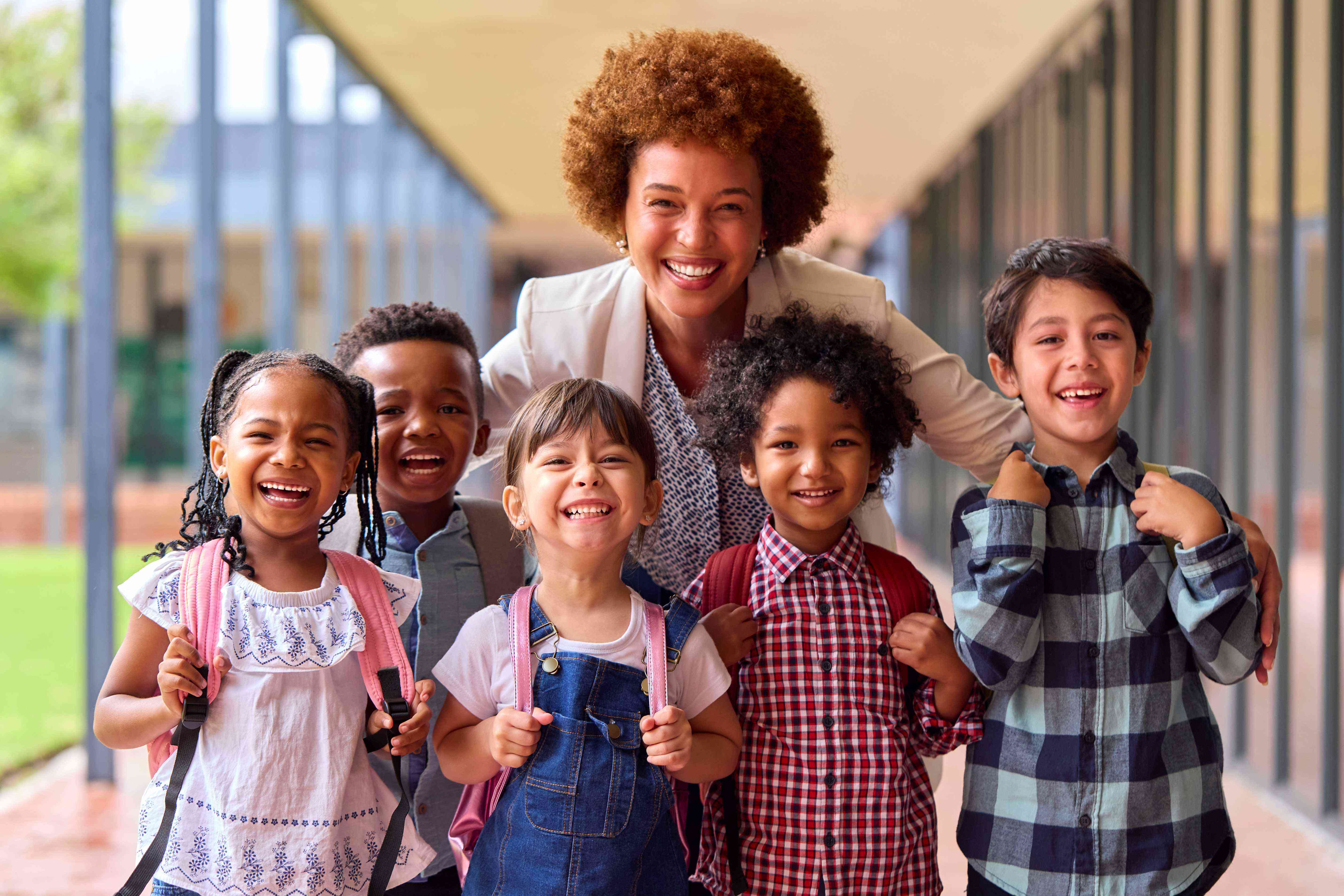 Children and their teacher gather together smiling outside a classroom