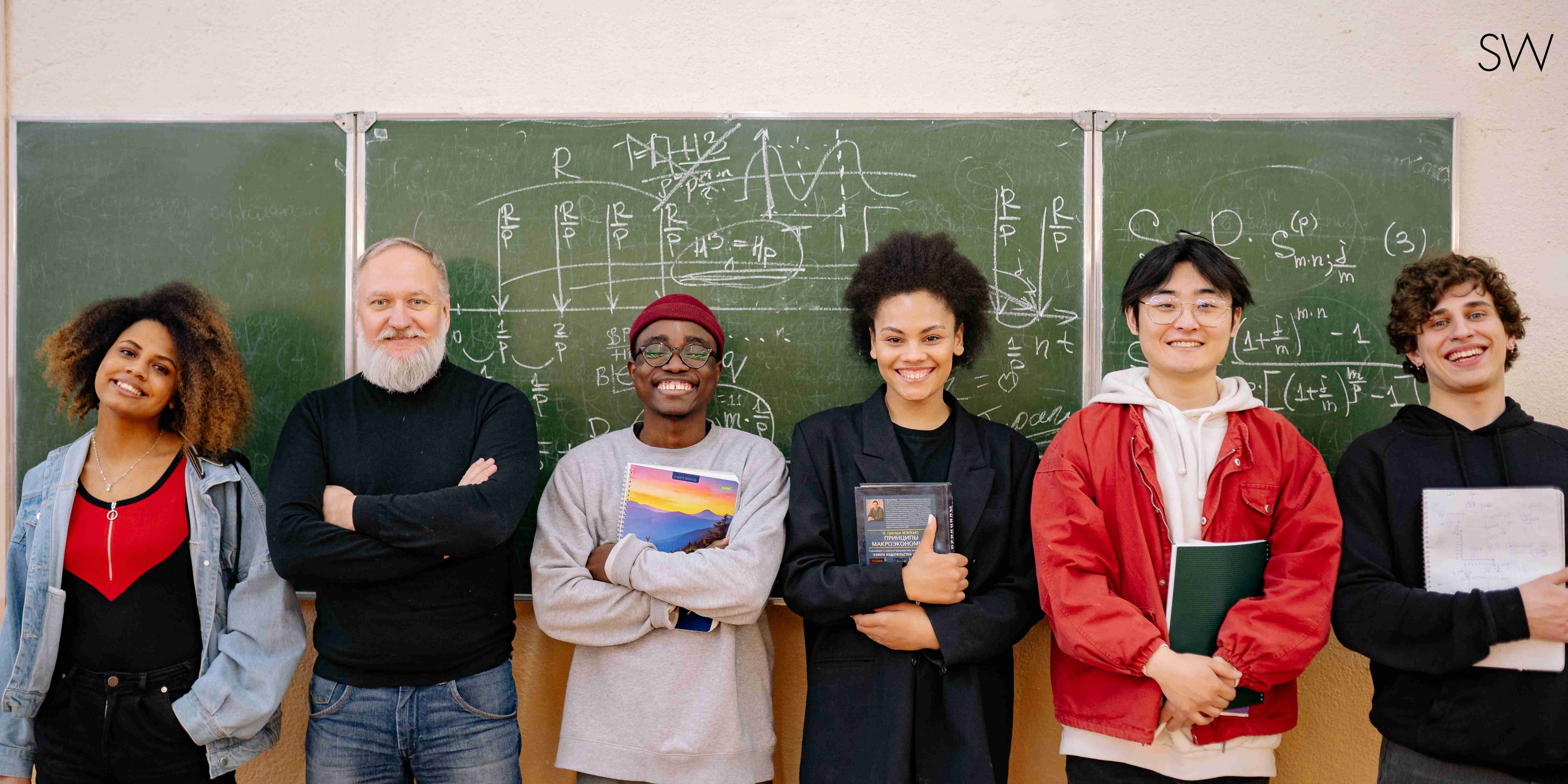multilingual students gather in front of a chalkboard with their teacher for a photo